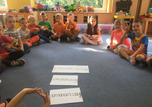 Dzieci siedząc na dywanie liczą litery, samogłoski, spółgłoski w wyrazie pomarańczowy.
