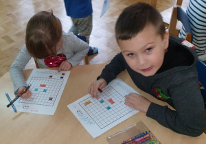 Dzieci rozwiązują dyktando graficzne przy stolikach.