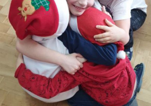 Chłopcy w czapkach św. Mikołaja przytulają się podczas tańca.