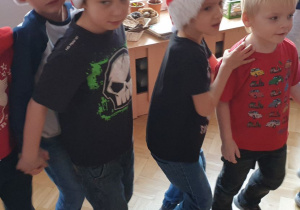 Chłopcy w czapkach św. Mikołaja tańczą w wężyku.