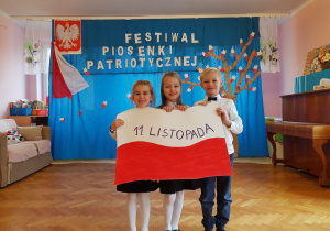 Tosia, Natalka i Patryk trzymają flagę Polski.