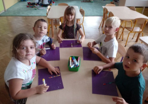 Dzieci siedzą przy stoliku i dekorują patyczki.