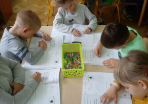 Dzieci kolorują ilustrację w ksiażce przedstawiającą papugę.