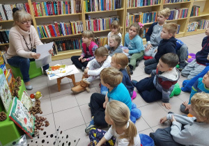 Dzieci słuchają opowiadania czytanego przez panią bibliotekarkę.