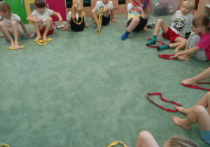 Dzieci próbują chwycić stopami szarfy gimnastyczne.