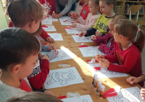 Dzieci wyklejają szablon Św Mikołaja bibułą.
