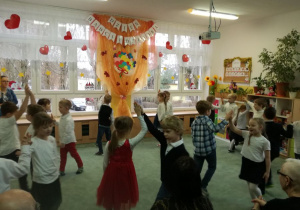 Dzieci tańczą w parach trzymając się za ręce uniesionymi w górze.
