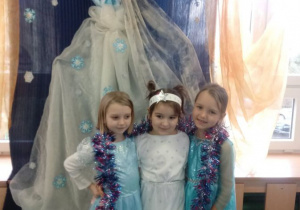 Dziewczynki prezentują swoje stroje na tle zimowej dekoracji.