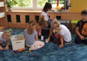 Dzieci siedząc na dywanie układają budowle z klocków.