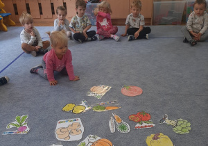 Dzieci siedząc w kole oglądają rysunki różnych warzyw.