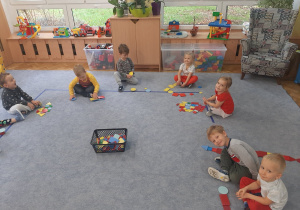 Dzieci siedzą na dywanie i układają z figur geometrycznych.