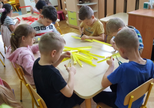 Dzieci siedzą przy stole. Nacinają paski papieru.