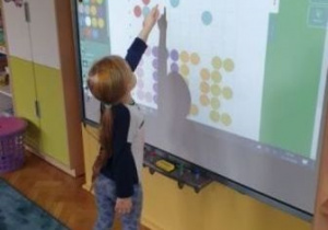 Dziewczynka stojąc przy tablicy interaktywnej rozkodowuje wzór na wirtualnej macie.