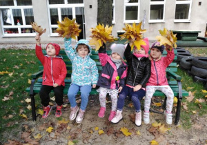 Dziewczynki siedzą na ławce w ogrodzie przedszkolnym i w ręku trzymają bukiet z liści.