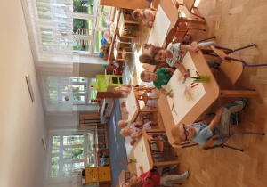 Dzieci przy stolikach rysują prace plastyczne.