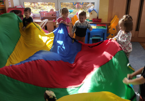 Dzieci falują chustą animacyjną podrzucając jeżyka- maskotkę.