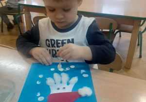 Chłopiec stempluje patyczkiem białe kropki tworząc śnieg.