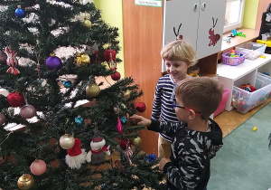 Piotruś i Mikołaj oglądają zwieszony ozdoby na choince.