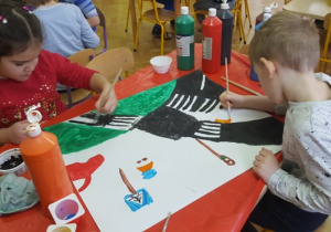 Dzieci malują farbami kolejne elementy pracy grupowej.