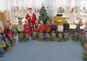 Wszystkie dzieci stoją razem ze Św. Mikołajem, zadowolone z otrzymanych upominków.