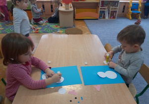 Dwójka dzieci nakleja elementy bałwana na kartkę.