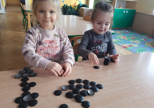Dwie dziewczynki układają wzory z guzików przy stole.