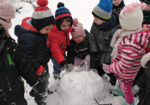 Dzieci lepią wspólnie wielką kule śniegową.