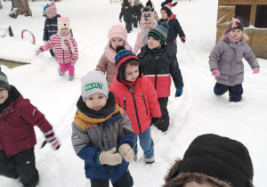 Dzieci biegają po zaśnieżonym ogrodzie.