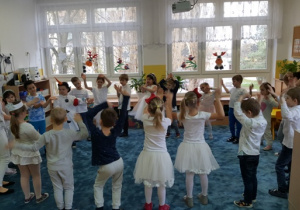 Dzieci tańczą w dużym kole z rękami uniesionymi w górę.