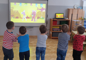 Dzieci tańczą piosnkę "Baby shark" naśladując ruchy wyświetalne na tablicy interaktywenej.