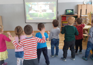 Dzieci tańczą piosnkę "Five litte monkeys" naśladując ruchy wyświetalne na tablicy interaktywenej.