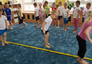 Dzieci przeskakują obunóż przez laski ułożone w jednej linii.