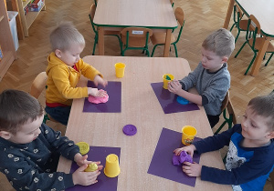 Dzieci przy stoliku lepią kształty z ciastoliny.