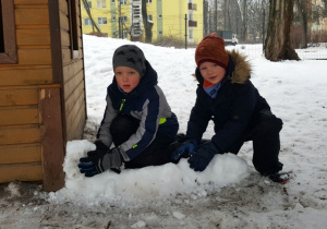Wiktor i Tomek rozpoczęli budowę śnieżnej fortecy obok drewnianego domku.