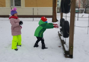 Olek i Naila ćwiczą celność rzucając śnieżkami w powieszone na drabince opony.