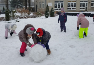 Dzieci toczą śnieżne kule. Chcą wspólnie ulepić dużego bałwana.