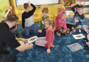 Dzieci siedzą na dywanie w zespołach rówieśniczych, układają strażackie puzzle.