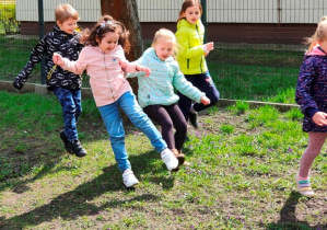 Dzieci grają w piłkę kopiąc ją po trawie.