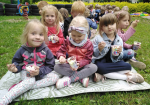 Dzieci siedzą na kocu i zajadają pyszne lody.