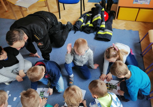 Dzieci siedzą na niebieskim dywanie i układają obrazek strażaka