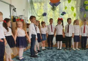 Dzieci stojąc w półkolu podają sobie ręce- szykują się do zaśpiewania piosenki okolicznościowej.
