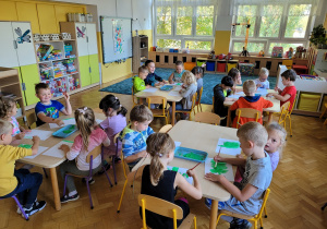 Dzieci siedzą przy stolikach i malują pracę plastyczną.