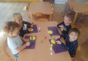 Dzieci siedzą przy stoliku i tworzą pszczółki z papieru do kodeksu.