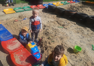 Trzech chłopców bawi się w piaskownicy samochodem.