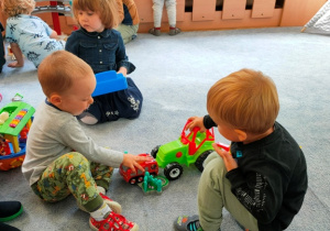 Dwóch chłopców bawi się autami na dywanie.