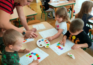 Dzieci siedzą przy stolikach- malują palcem kolorowe kropki na kartonie.