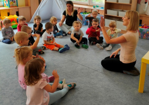 Dzieci siedząc na dywanie - ciocia Ania śpiewa im nową piosenkę.