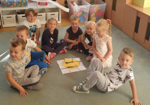 Dzieci siedzą na dywanie i prezentują efekt swojej pracy.