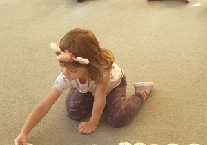 Dziewczynka układa na dywanie odpowiedni element domina.