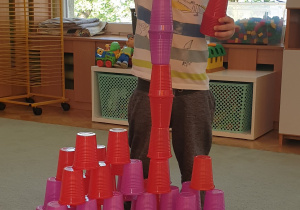 Chłopiec układa wieże z kolorowych kubeczków.
